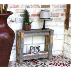 a wooden table with a lamp on it next to a brick wall and a potted plant