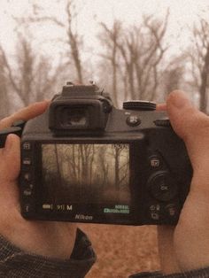 a person holding up a camera to take a photo in front of some bare trees