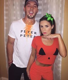 a man standing next to a woman in front of a wall with a pumpkin on it