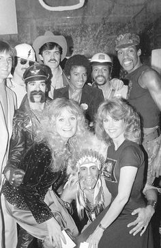 a group of people posing for a photo in front of an audience wearing costumes and wigs