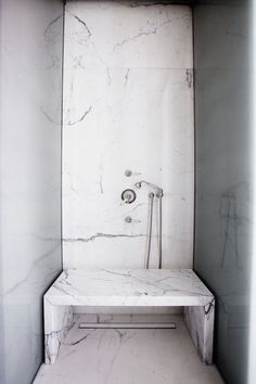 a bathroom with marble walls and flooring, including a shower head in the corner