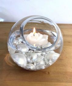 a glass bowl filled with white rocks and a lit candle in it on top of a wooden table