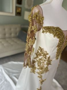 a white dress with gold sequins is on display in a room next to a couch