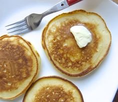 three pancakes on a plate with butter and a fork