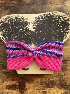 a pink and purple knitted hair bow on top of a piece of cardboard paper