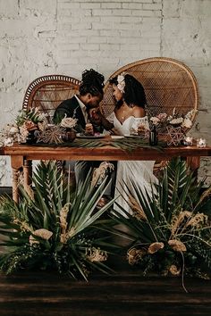 a bride and groom sitting at a table surrounded by greenery