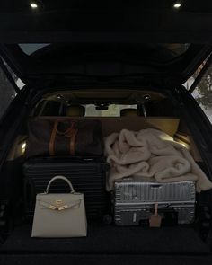 two suitcases are sitting in the back of a car with blankets and bags on it