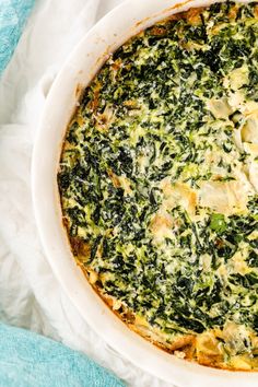 a spinach and cheese casserole in a white dish on a blue towel