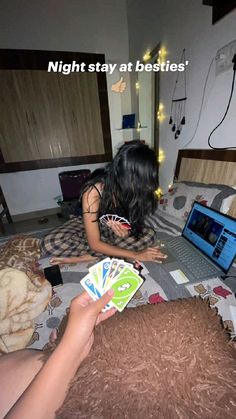 a woman sitting on top of a bed next to a laptop computer and playing cards