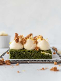 a piece of green cake with white icing and walnuts on top, sitting on a glass plate