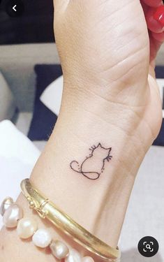 a woman's wrist with a cat tattoo on it and pearls around the wrist