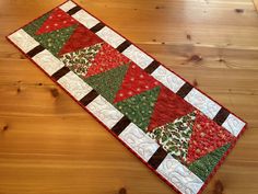 a table runner made with red, green and white christmas quilts on a wooden floor