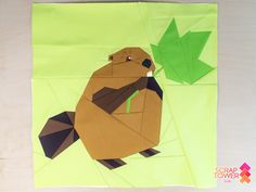 an animal made out of paper sitting on top of a wooden table next to a green leaf