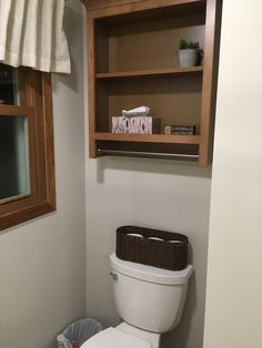 a white toilet sitting in a bathroom next to a wooden shelf filled with boxes and towels