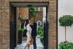 a man and woman kissing in front of an open door with potted plants on either side