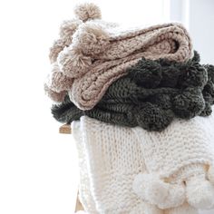 a pile of knitted blankets sitting on top of a wooden chair next to a window