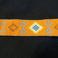 an orange beaded bracelet with blue and yellow designs on it's side, sitting on a black surface