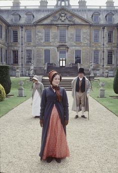 a woman standing in front of a large building with two men walking behind her on the other side