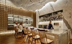 people are sitting at the bar in an elegant restaurant with marble walls and wooden chairs