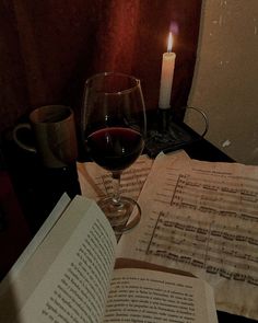 a glass of wine and an open book on a table with sheet music paper next to it