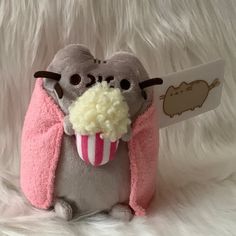 a stuffed animal with a pink and white scarf around it's neck holding a cupcake in its mouth