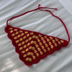 a crocheted red and gold triangle on a white bed with the string down