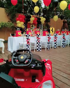 a red toy car parked in front of a table filled with yellow and black balloons