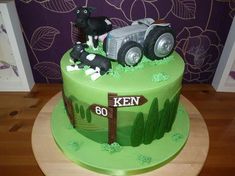 a green cake with a tractor and farm animals on it's side, sitting on a wooden table