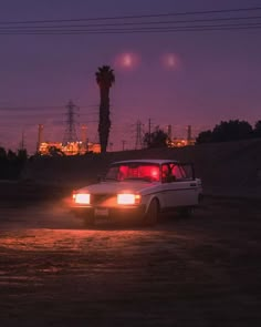 a white car parked on top of a dirt field next to power lines at night