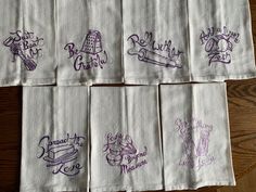 six embroidered napkins with purple ink on them sitting on top of a wooden table