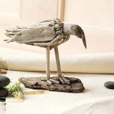 a bird made out of driftwood sitting on top of a table next to rocks