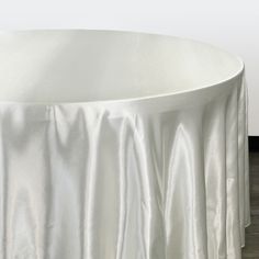 a round table with white cloth draped over it on top of a hard wood floor