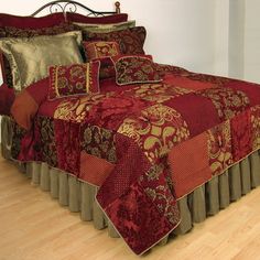 a bed with red and gold bedspread on top of wooden floor next to white wall