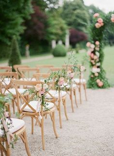 rows of chairs with flowers on them in front of an outdoor wedding ceremony arch at the end of a gravel path