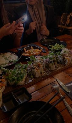 two women sitting at a table looking at their cell phones with food on the table