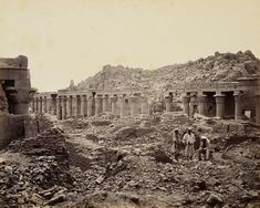 an old photo of some people standing in the dirt near ruins and buildings with large pillars