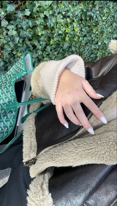 a woman's hand on top of a black leather jacket with white nails and a green purse