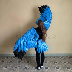 a woman standing in front of a wall wearing a blue and black feathered bird costume