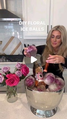 a woman pouring wine into a bowl filled with iceballs and roses in a kitchen