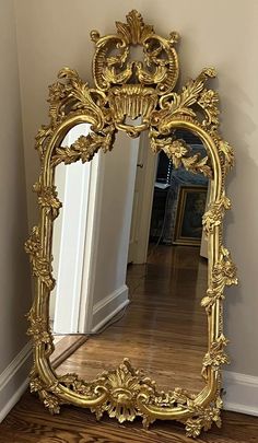 an ornate gold framed mirror sitting on top of a hard wood floor next to a wall