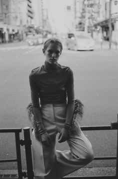 black and white photograph of a woman sitting on a fence in the street with her hands behind her back