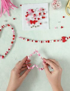 two hands are making beaded hearts with beads and other crafting supplies on a table