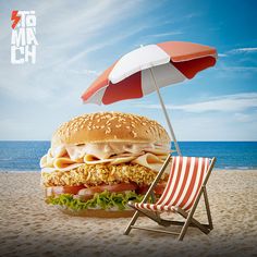 a large hamburger sitting on top of a sandy beach next to an orange and white umbrella