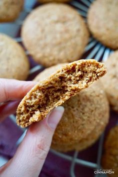 a hand holding a cookie in front of some muffins on a cooling rack