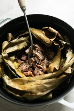 the food is being cooked in the pot with tongs and some sort of utensil