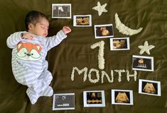 a baby laying on top of a blanket covered in pictures and writing that reads 1 month