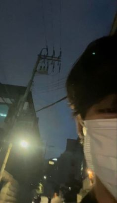 a person wearing a face mask and holding a cell phone up to their ear while standing in the street at night