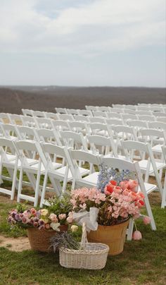 an outdoor ceremony set up with white chairs and flower baskets on the grass in front of them