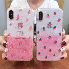 a woman holding two iphone cases with pink glitter and strawberrys on them in front of a wooden table