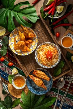 two plates filled with food on top of a wooden table next to bowls of sauce